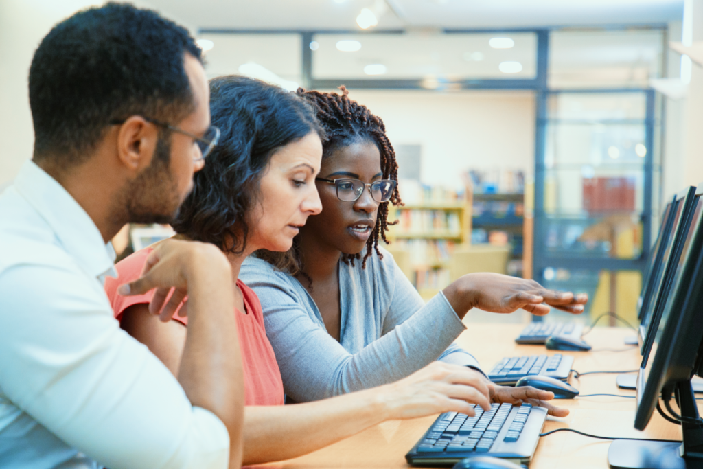 Two women and a man working in a computer, actively debating while looking into the screen