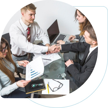 Two men shaking hands across a desk, while two woman next to them are taking notes and looking through data